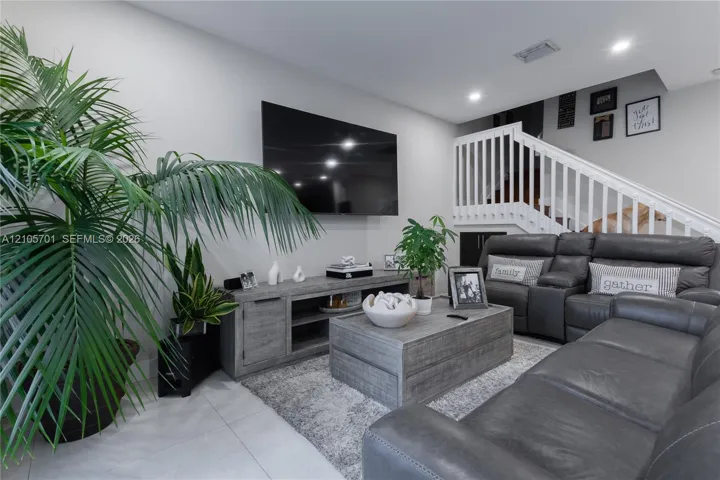 Neutral-toned interior featuring large-format tile flooring, recessed lighting, and a white staircase with a classic balustrade