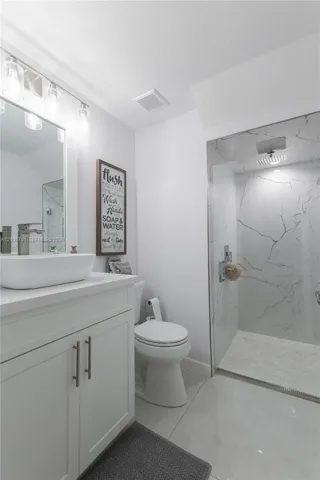 Bathroom featuring a vanity with a white vessel sink, polished chrome faucet, glass-enclosed shower with large-format tile surround, and tile flooring