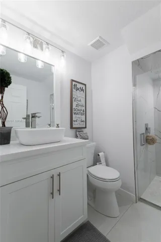 White vanity featuring a rectangular vessel sink with chrome faucet, topped with a solid surface counter and accompanied by a walk-in shower with floor-to-ceiling tile surround and a glass door
