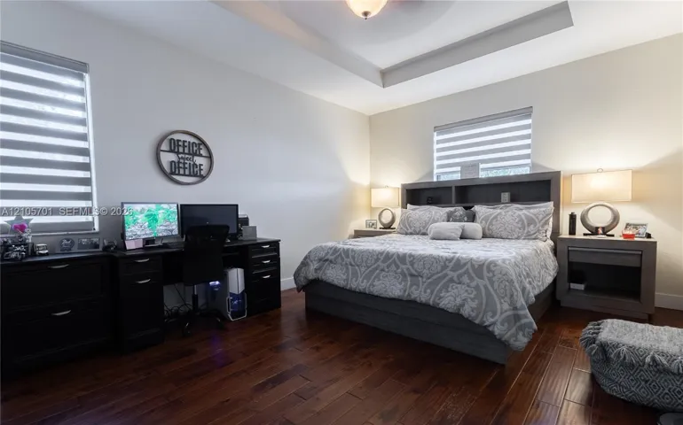 Tray ceiling, wood-finish flooring, and dual windows featuring adjustable roller shades