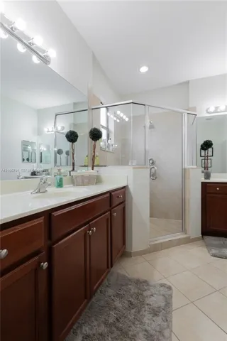 Dual-sink vanity with dark wood cabinetry and solid-surface countertops, large frameless vanity mirrors, and a tiled walk-in shower with glass enclosure