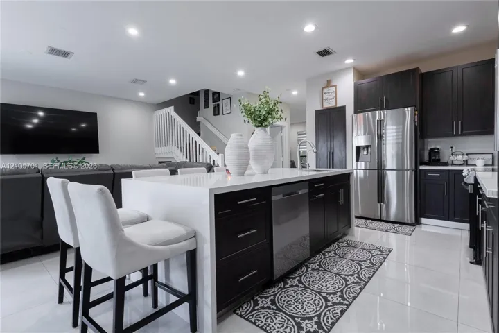 Kitchen featuring dark-finish cabinetry, an island with a white solid-surface countertop, stainless steel appliances, and large-format tile flooring