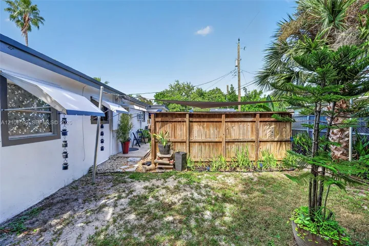 Private outdoor space featuring a wood perimeter fence, retractable sun shade, wall-mounted window awnings, and established landscaping