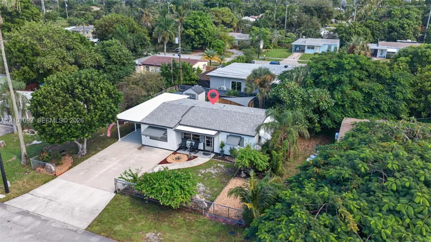 Single-story residence featuring a shingle roof, attached carport, concrete driveway, metal window awnings, and landscaped exterior grounds