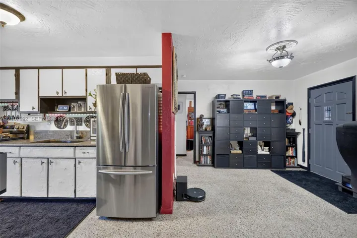 Kitchen featuring white cabinetry, solid surface countertops, and a stainless steel French-door refrigerator, complemented by ceiling-mounted light fixtures and an exterior entry door