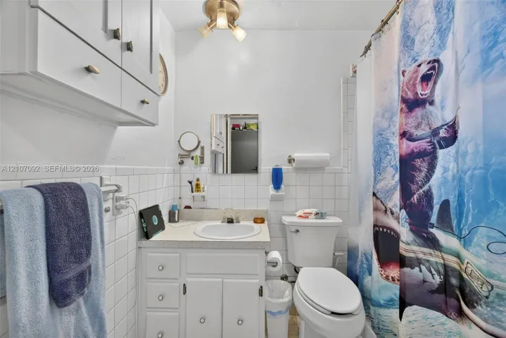 Bathroom featuring white ceramic wall tile, a built-in vanity with integrated basin, upper wall-mounted cabinetry, and a three-light fixture