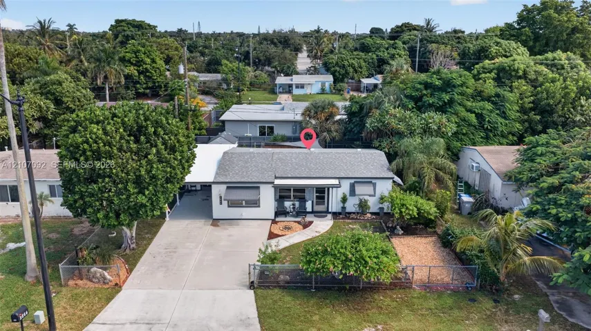 Single-story residence featuring a concrete driveway, attached carport, metal awnings, fenced front yard, and mature landscaping