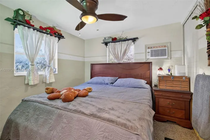 Bedroom featuring dual windows, ceiling fan with integrated lighting, wall-mounted air conditioning unit, and sliding closet doors