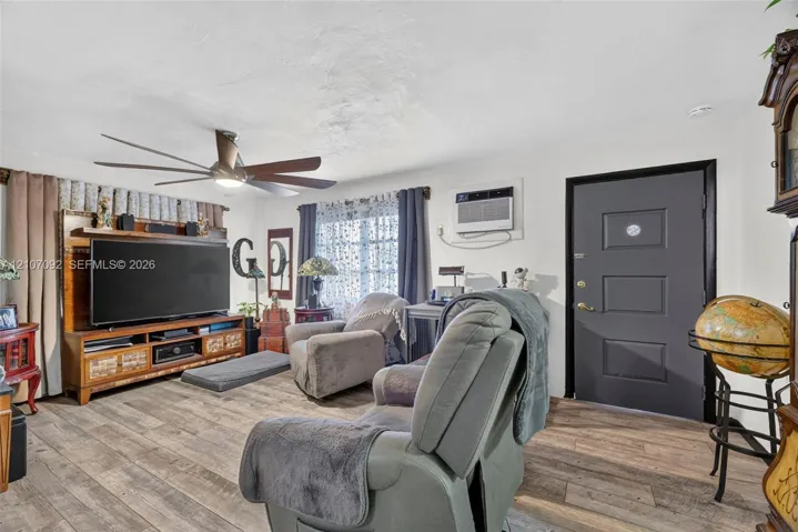 Living area featuring wood-finish flooring, a multi-blade ceiling fan, and a dark-toned paneled entry door