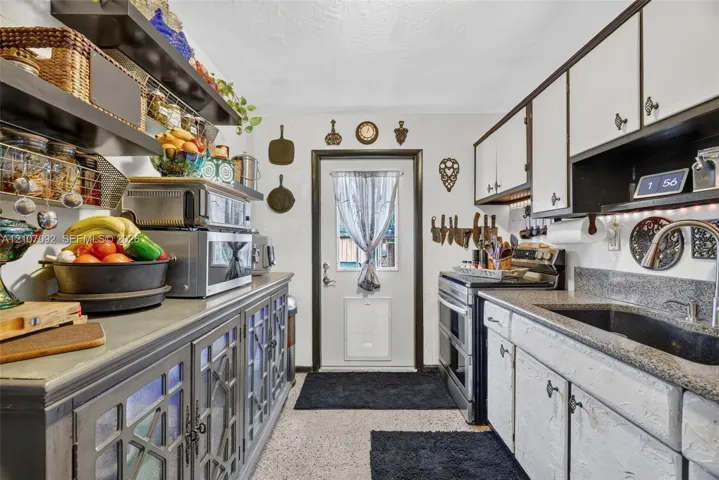 Kitchen featuring two-tone cabinetry with glass-panel doors, dark stone-finish countertops, an undermount sink with a gooseneck faucet, open shelving, and a glass-paneled exterior door