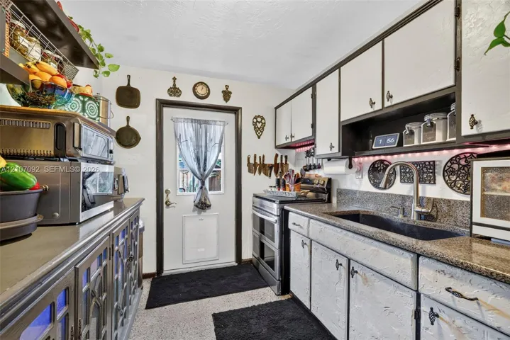 Kitchen featuring stone-finish countertops, an undermount sink with a high-arch faucet, custom cabinetry with glass-panel detailing, and an exterior entry door