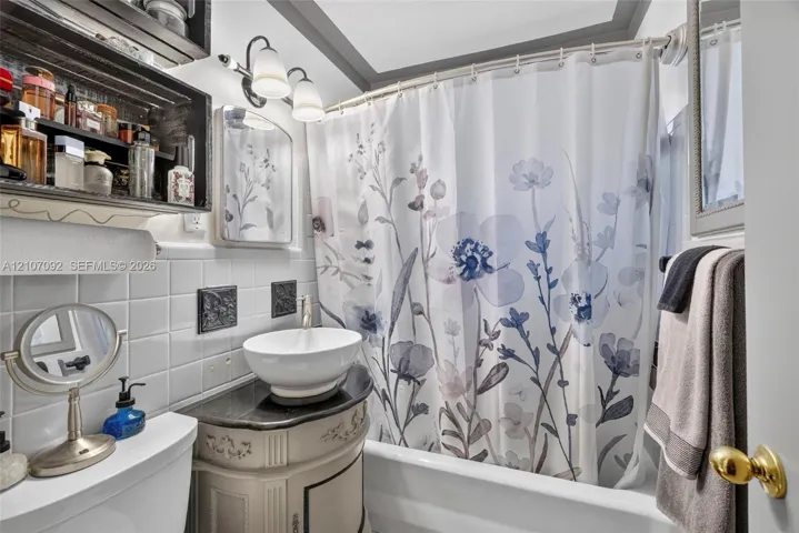Bathroom featuring a vessel sink with a dark stone-finish countertop, white square wall tile, built-in shelving, and dual-bulb vanity lighting