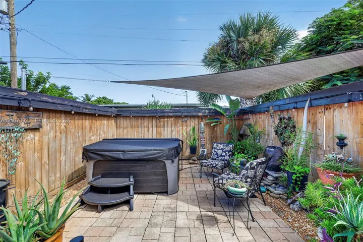 Private outdoor space featuring a paved patio, high wood-plank fencing, built-in hot tub, and overhead shade sail