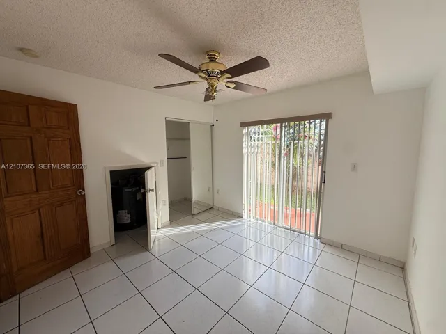 Room featuring tile flooring, sliding glass door with vertical blinds, mirrored closet, ceiling fan, and six-panel wood door