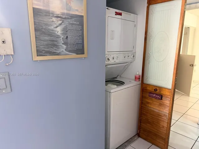 Stacked laundry unit featuring a white finish, enclosed by a wood-framed door with a frosted glass panel and decorative etching, set against tile flooring