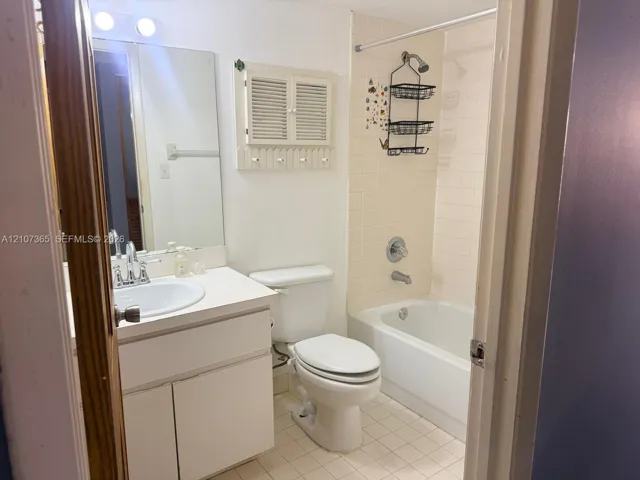 Bathroom featuring a white vanity cabinet with an integrated sink, wall-mounted medicine cabinet with louvered doors, oversized vanity mirror, and a tub-shower combination with tile surround