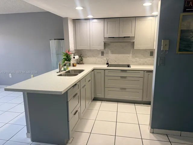 Kitchen featuring light gray shaker-style cabinetry, quartz countertops, a dual-basin stainless steel sink, a smooth-top electric cooktop, and tile flooring