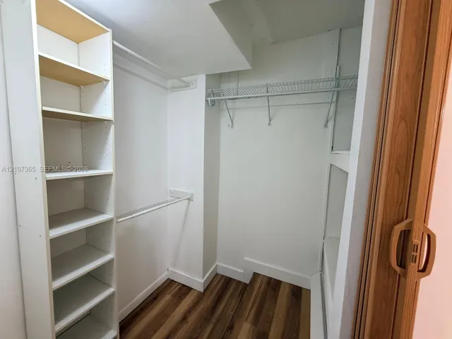 Walk-in closet featuring wood-finish flooring, built-in shelving unit, dual-level garment rods, wire storage shelving, and bi-fold door entry