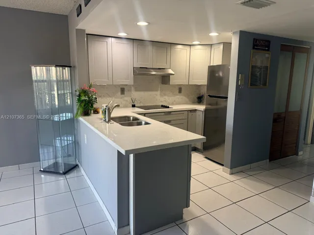 Kitchen featuring light-toned shaker cabinetry, stone-finish countertops, stainless steel appliances, a peninsula with an undermount dual-basin sink, and tile flooring