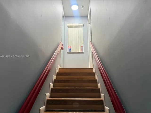 Staircase featuring wood-finish treads, dual wood-tone handrails, and a vertical blind window treatment