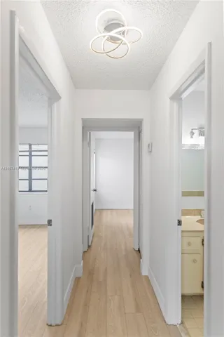 Hallway featuring wood-finish flooring, textured ceiling, contemporary circular flush-mount light fixture, and door-entry access to multiple rooms