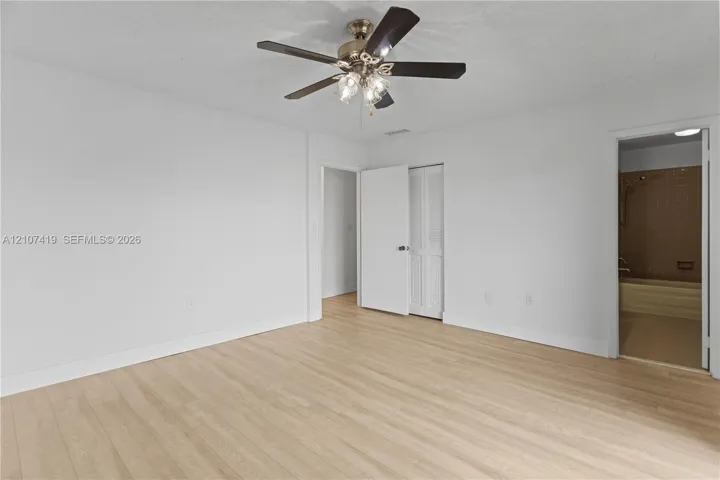 Interior space featuring light-toned wood-finish flooring, a multi-blade ceiling fan with integrated light fixture, and bifold closet doors