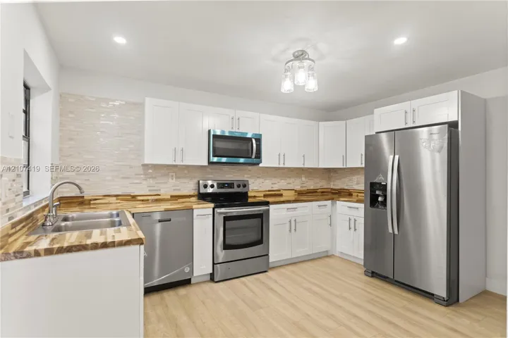 Kitchen featuring white cabinetry, butcher block countertops, stainless steel appliances, a tile backsplash, and wood-finish flooring