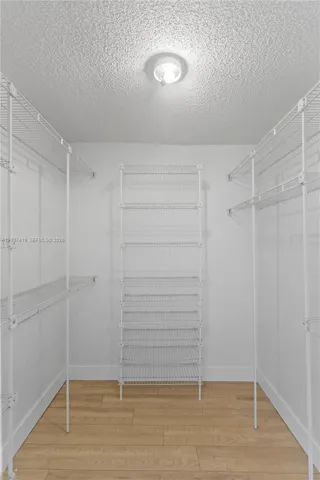 Walk-in closet featuring white wire shelving units and wood-finish flooring