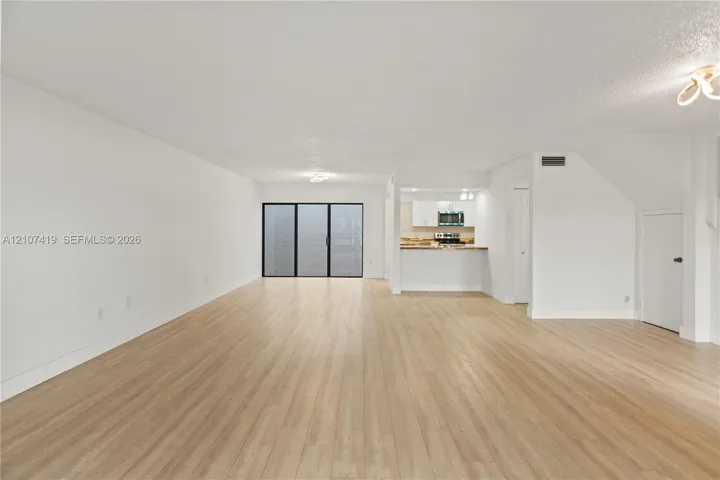 Open-concept interior featuring light-tone wood-finish flooring, white cabinetry, a kitchen pass-through counter, and a glass sliding door system