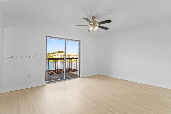 Room featuring wood-finish flooring, a ceiling fan with integrated lighting, and a sliding glass door providing access to a balcony with metal railing