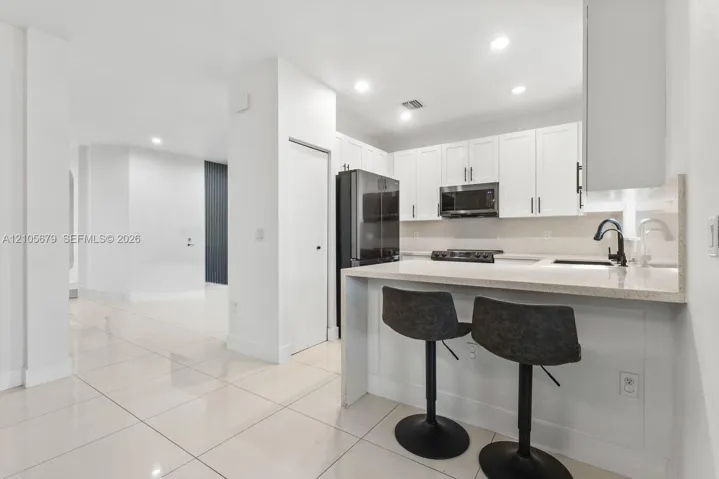 Kitchen featuring white shaker-style cabinetry, a stone-surface breakfast bar, recessed lighting, and tile flooring