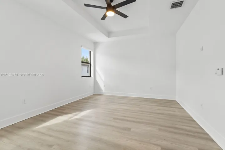 Interior space featuring a recessed tray ceiling, wood-finish flooring, and a central ceiling fan with integrated lighting