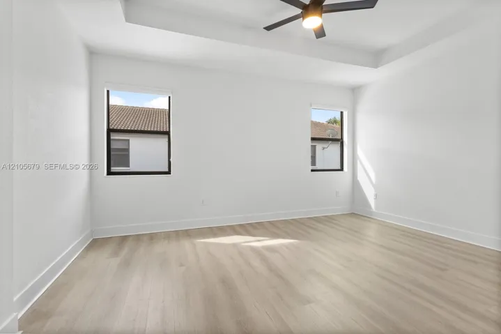 Room featuring tray ceilings, wood-finish flooring, dual windows with dark frames, and a central ceiling fan with integrated lighting
