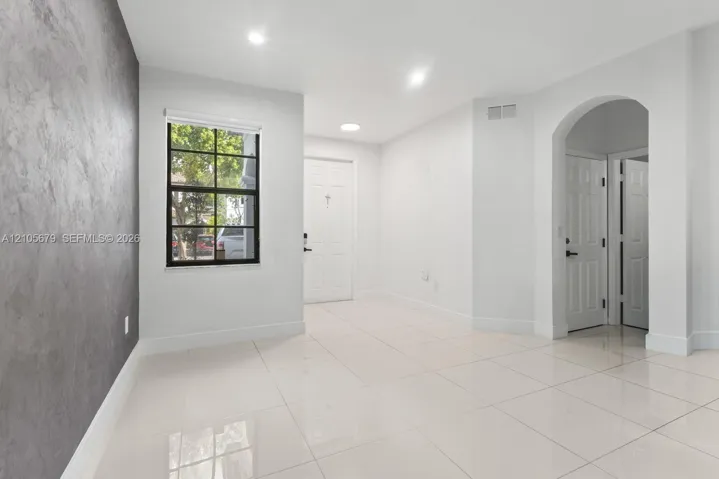 Interior space featuring a textured gray accent wall, large-format tile flooring, recessed lighting, a grid-pane window, and a prominent arched entryway
