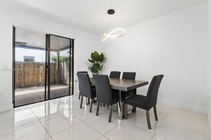 Large-format neutral tile flooring, modern sculptural pendant lighting, and oversized sliding glass doors leading to a paved patio area