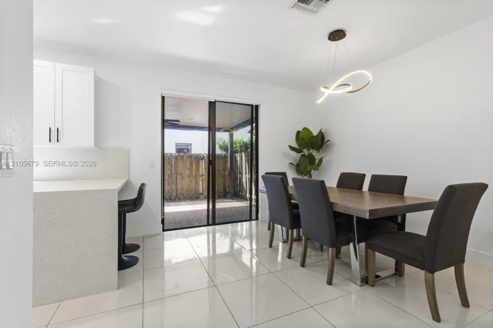 Polished porcelain flooring, quartz breakfast bar, white cabinetry, architectural LED pendant lighting, and sliding glass patio doors