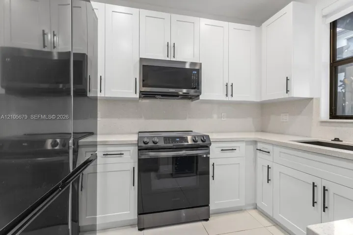 Kitchen featuring white shaker-style cabinetry, solid-surface countertops, stone-finish backsplash, and stainless steel appliances including a built-in microwave and range