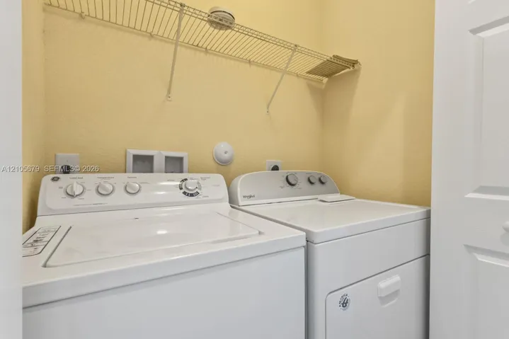 Utility space featuring white top-load washer and dryer units, integrated wall-mounted wire shelving, and recessed electrical and water hookups