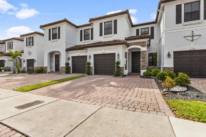 Two-story stucco facade with stone masonry accents, tile roofing, brick-paver driveways, and integrated garage doors