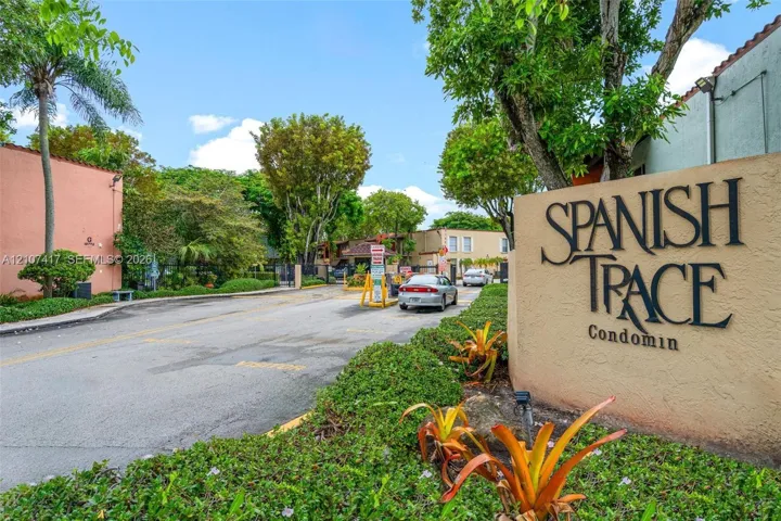 Community entrance featuring a gated access point, mature landscaping, and stucco signage