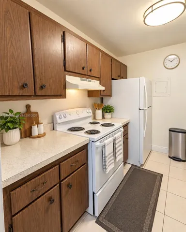 Kitchen featuring wood cabinetry, stone-finish countertops, tile flooring, and integrated white appliances including a range and refrigerator