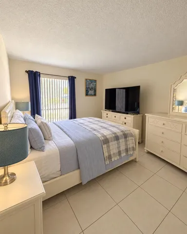 Neutral-toned ceramic tile flooring, textured ceiling, and large sliding glass door with vertical blinds