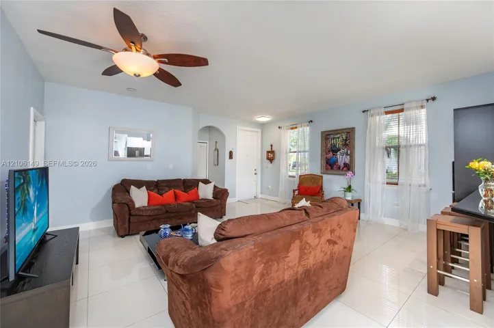 Living area featuring polished tile flooring, a five-blade ceiling fan with integrated light fixture, and an arched doorway