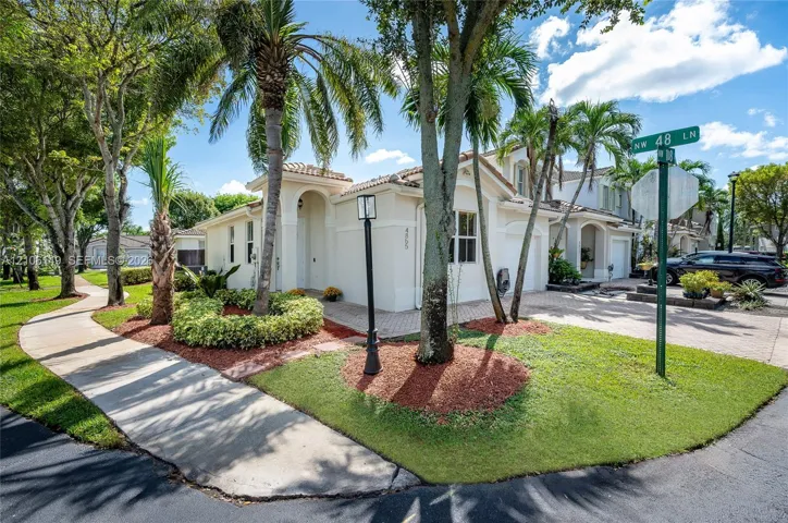 Stucco exterior featuring an arched entryway, paver driveway, integrated garage, and mature palm landscaping