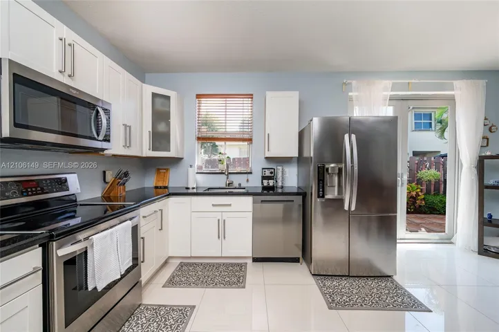 Kitchen featuring white shaker-style cabinetry, dark stone countertops, stainless steel appliances, polished tile flooring, and double glass doors