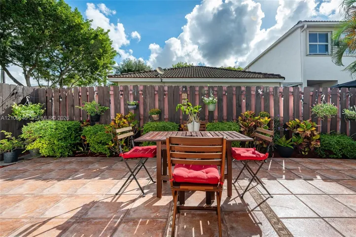 Private fenced patio featuring ceramic tile flooring, mature landscaping, and wall-mounted string lighting