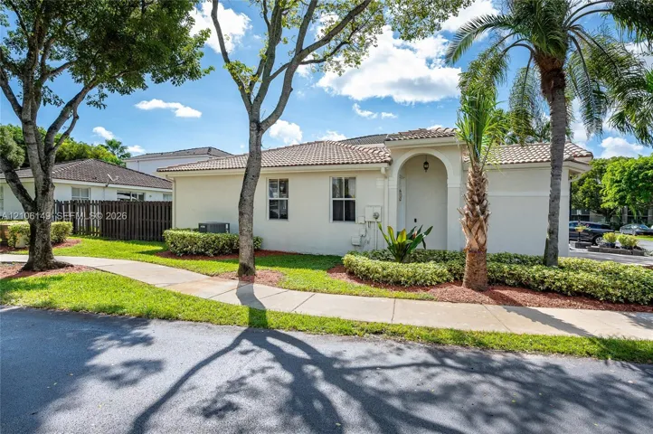 Stucco exterior featuring a tiled roof, arched entryway, and landscaped foundation gardens