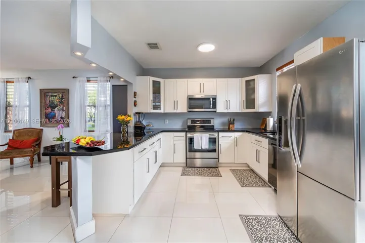 Kitchen featuring white shaker-style cabinetry, dark stone countertops, stainless steel appliances, and polished tile flooring
