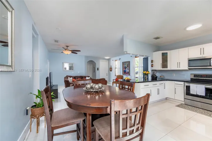 Open-concept kitchen featuring white shaker-style cabinetry, dark stone countertops, stainless steel appliances, and polished tile flooring