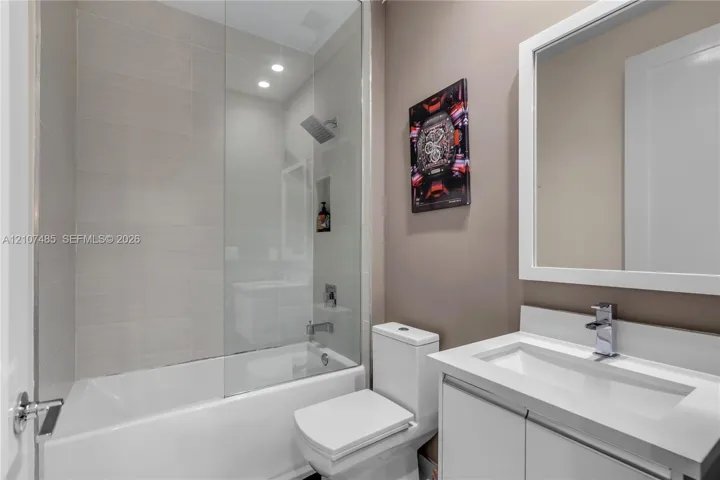 Bathroom featuring a white vanity with a rectangular sink, framed wall mirror, glass shower partition, tile-surround tub, and rainfall showerhead